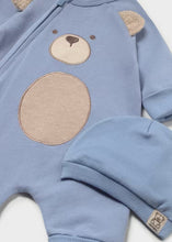 Load image into Gallery viewer, A light blue ribbed knit baby romper with a teddy bear face applique on the chest and matching ear patches, shown alongside a matching blue ribbed knit hat with a small embroidered bear patch.
