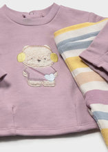 Load image into Gallery viewer, A close-up of a baby's dusty mauve long-sleeve top featuring an embroidered teddy bear applique on the chest, with a folded striped knit leggings in pastel yellow, blue, and cream tones placed next to it.