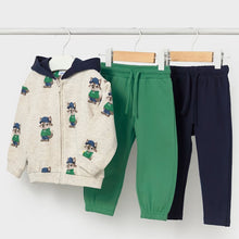 Load image into Gallery viewer, A three-piece children's clothing set hanging on a white rack: a zip-up hoodie in cream with a navy hood and colorful animal prints, green drawstring pants, and navy pants.
