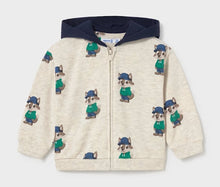 Load image into Gallery viewer, A child's zip-up hoodie with a cream-colored body, a navy blue hood, and an all-over print of cartoon raccoons wearing green sweaters and blue hats.
