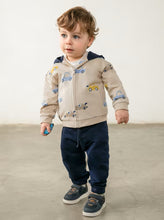 Load image into Gallery viewer, A toddler standing  wearing a beige zip-up hoodie with a car print, navy pants, and navy sneakers.
