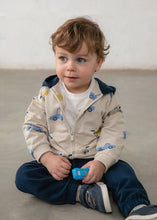 Load image into Gallery viewer, A toddler sitting on a floor wearing a beige zip-up hoodie with a blue car print, navy pants, and holding a small blue toy car.
