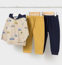 Load image into Gallery viewer, A children's three-piece clothing set hanging on wooden hangers against a white wall. The set includes a beige zip-up hoodie with a navy blue hood and a car print, a pair of mustard yellow jogger pants, and a pair of navy blue jogger pants.
