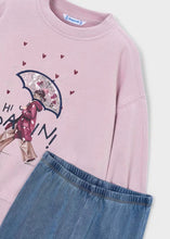 Load image into Gallery viewer, A close-up of a light pink crewneck sweatshirt featuring a graphic of a girl walking under a glittery umbrella with small red hearts and text, paired with blue denim pants.
