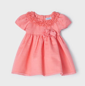 A beautiful dress for a baby or toddler girl in coral pink . High-waisted style . Short puff sleeves and  neckline  decorated with ruffles. Waist embellished with fabric bow two roses Net underneath. Centre back concealed zipper. Buy online kidstuff.ie Made by Mayoral