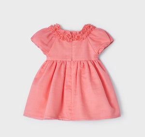 A beautiful dress for a baby or toddler girl in coral pink . High-waisted style . Short puff sleeves and neckline decorated with ruffles. Waist embellished with fabric bow two roses Net underneath. Centre back concealed zipper.  Mayoral 1908