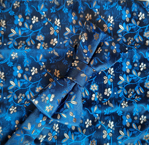 Boy's bow tie and pocket square in dark blue  brocade patterned with lighter blue and  gold in an all-over floral design. The necktie is on an adjustable band for a comfortable fit from about 7 years to 14 years and has a hook and bar fastening. Suitable for special occasions including First Communions and weddings. 