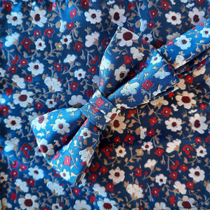 Boy's bow tie and pocket square dark blue brocade patterned with light grey, cherry red and a touch of tan in a tiny  all-over floral design. The necktie is on an adjustable band for a comfortable fit from about 7 years to 14 years and has a hook and bar fastening. Suitable for special occasions including First Communions and weddings.