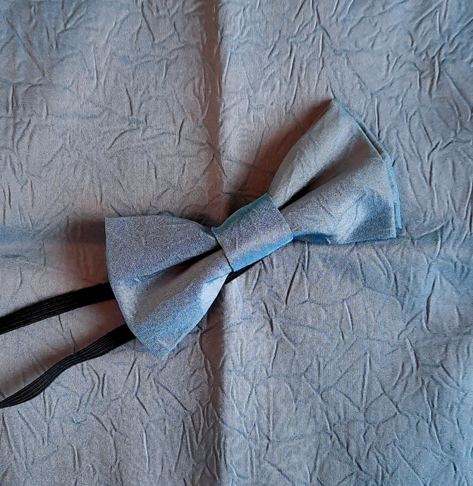 Boy's bow tie and pocket square in blue/grey shot taffeta with a crinkle effect. The necktie is on an elastic band for a comfortable fit from about 7 years to 10 years. The pocket square is double faced. Suitable for special occasions including First Communions and weddings.